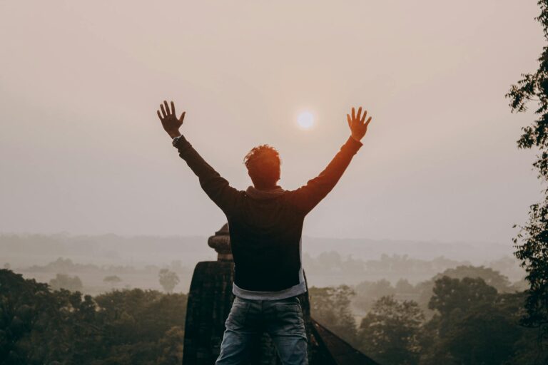 A man with outstretched arms stands against a sunrise in Odisha, India, symbolizing freedom and serenity.