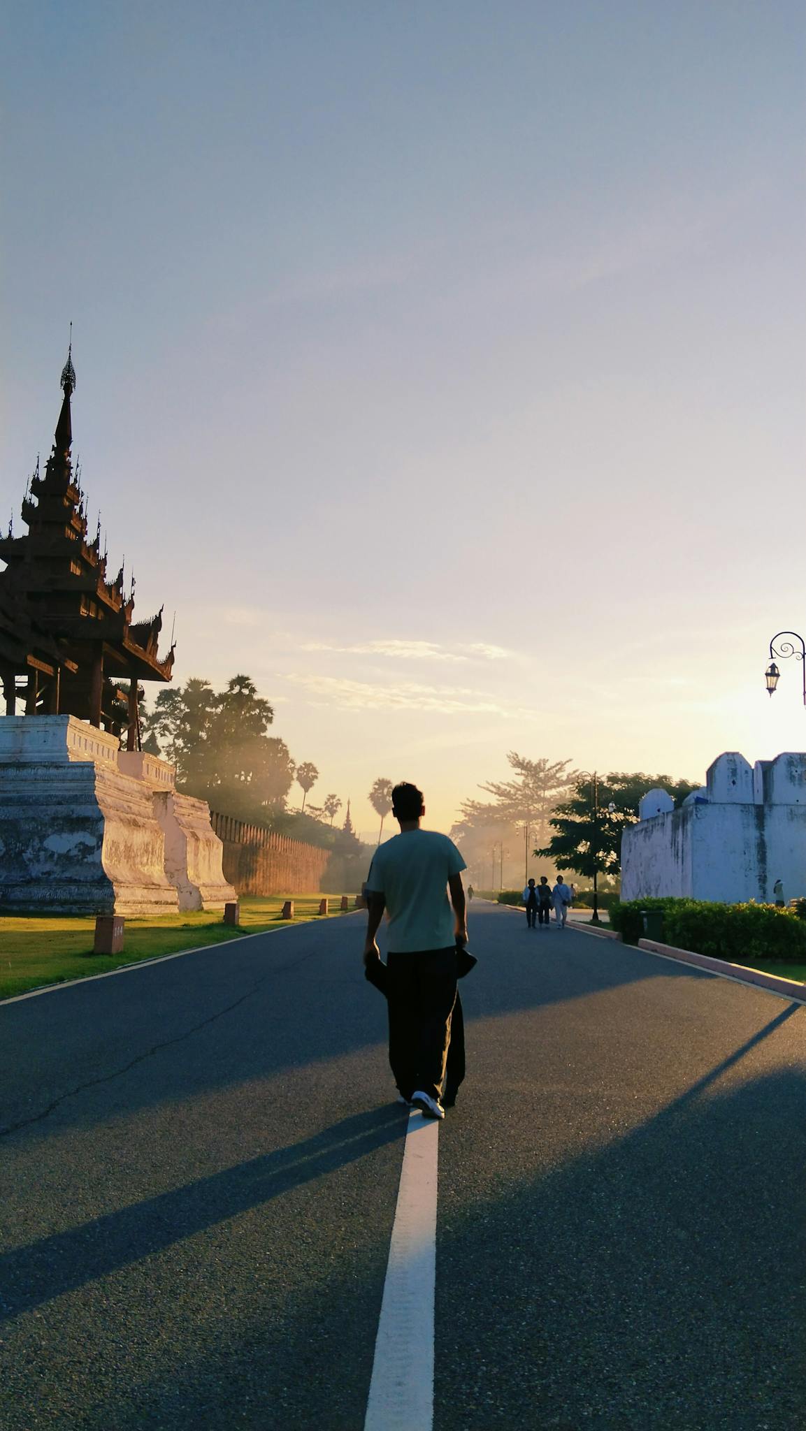 A person walking on a road near a traditional Asian structure at sunrise, capturing a serene morning vibe.