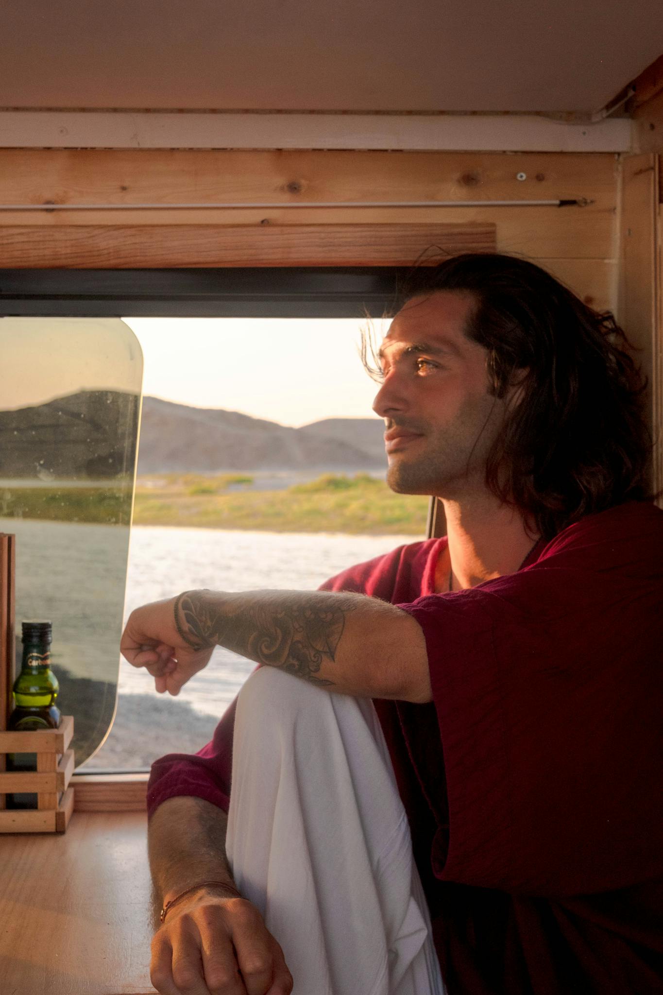 A reflective man sitting in a van, enjoying a serene landscape view through the window.