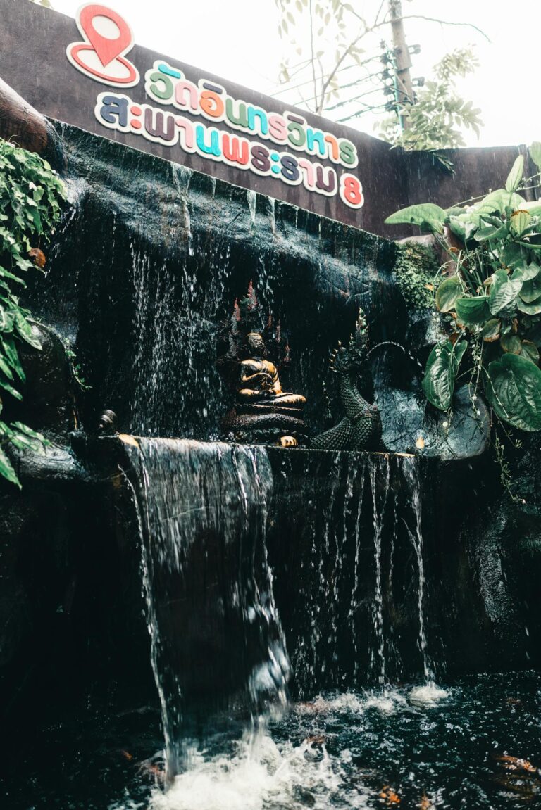 A tranquil Buddha statue near a waterfall in a Bangkok temple setting.